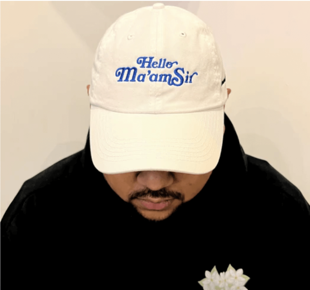A white baseball cap sold by Kalamansi Collective is shown with blue stitching with the words "Hello Ma'amSir" on it.