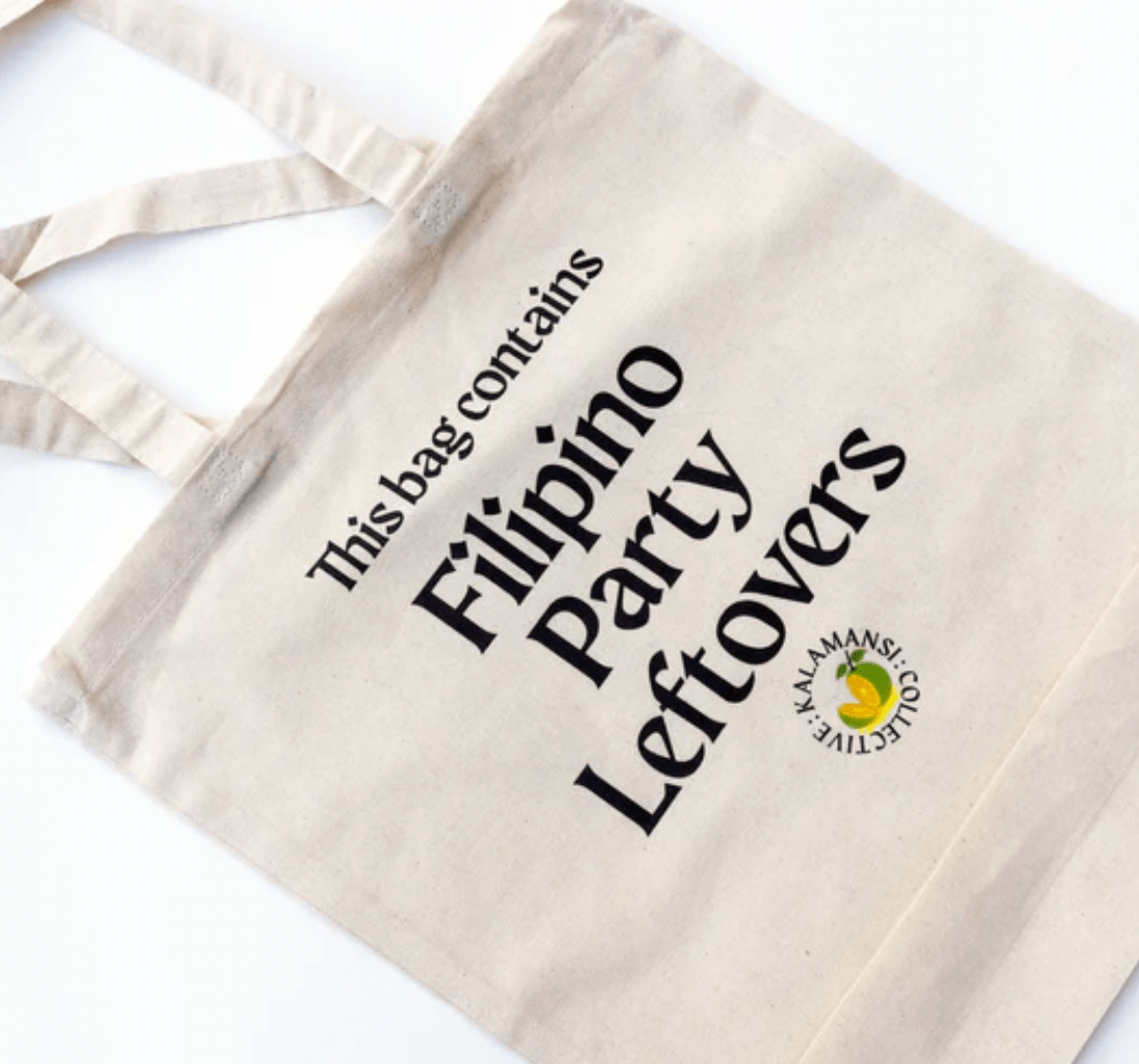 A white canvas tote bag from Kalamansi Collective with the words This bag contains Filipino Party Leftovers.