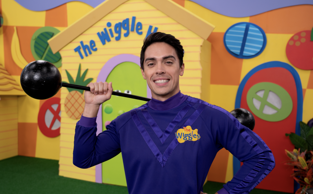 A photograph of John Pearce, the Purple Wiggle in The Wiggles, holding his weights while standing in front of The Wiggle House.